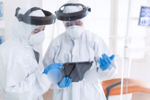 Dentists in dental office dressed in ppe suit using tablet pc