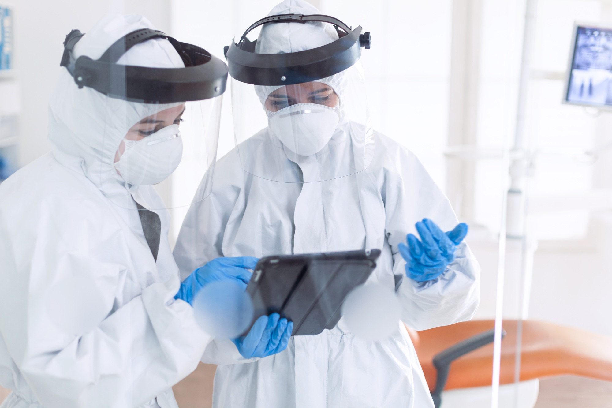 Dentists in dental office dressed in ppe suit using tablet pc